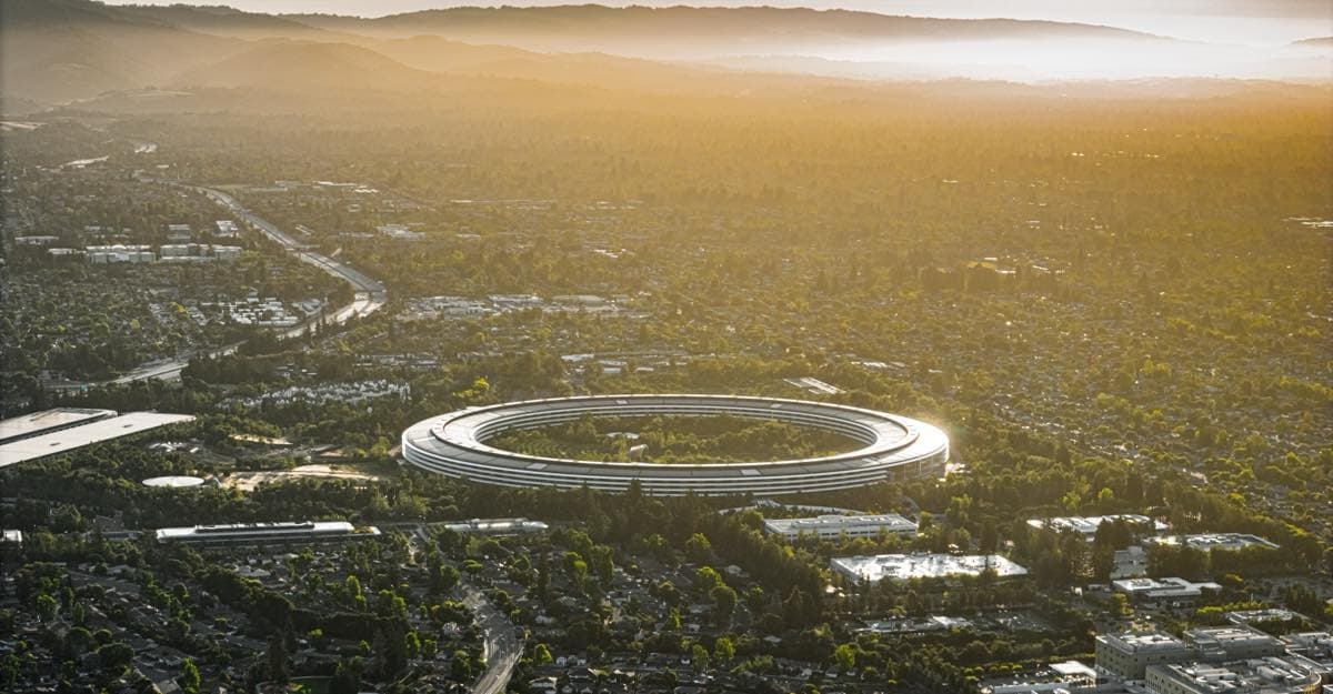 Aerial view of Apple Park, Apple's headquarters in Cupertino, California, at sunset, with the ring-shaped building surrounded by trees and hills