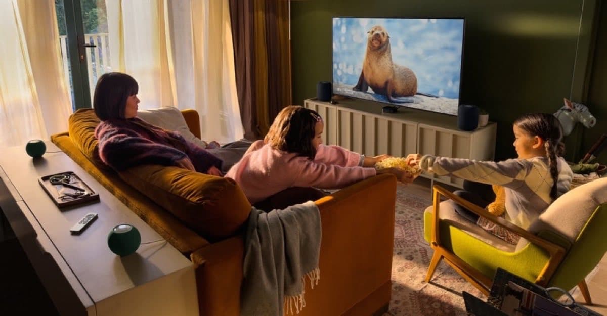 A warm living room with a family watching a nature documentary on a TV, with HomePod mini speakers around the screen