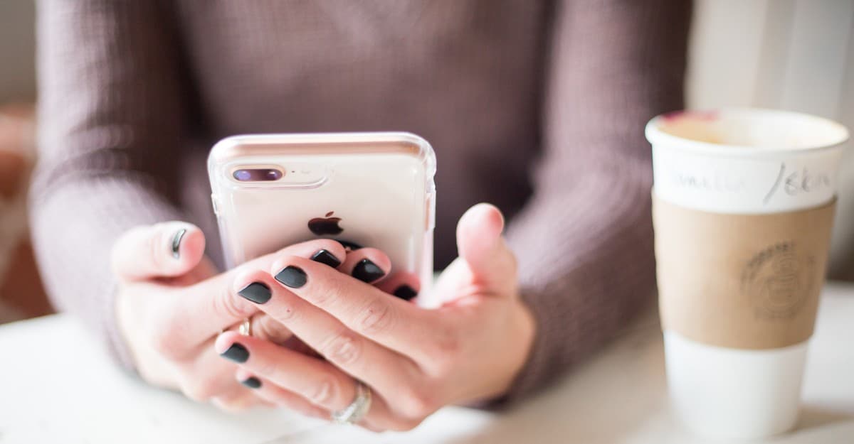 Woman holding an iPhone in a clear case, with a coffee cup on the table